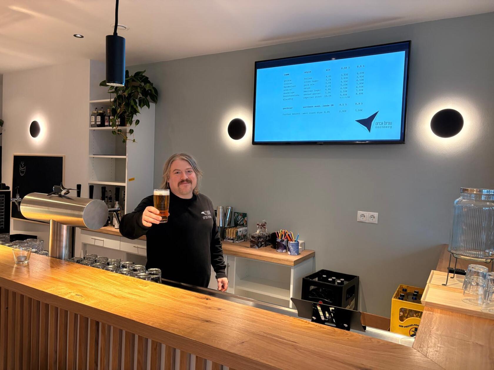 Nach Verzögerung konnten Fritz Großkopf und Orca Brau erstmalig die Türen der Orca-Bier-Bar öffnen. Fans des Bieres sind hier an der richtigen Adresse. Für Nicht-Biertrinkende gibt es eine Cola-Mix-Karte sowie weitere anti-alkoholische Getränke. Parallel dazu steht ein "Bottleshop" zur Verfügung. Das ist ein Kühlschrank, aus dem Gäste Flaschen aus dem Orca-Sortiment mitnehmen können. Eine Küche serviert drei verschiedene Flammkuchen, die im Angebot von Nüssen oder Chips flankiert werden. Neben der klassischen und der veganen Variante landen auch Nürnberger Rostbratwürste auf dem Flammkuchen.