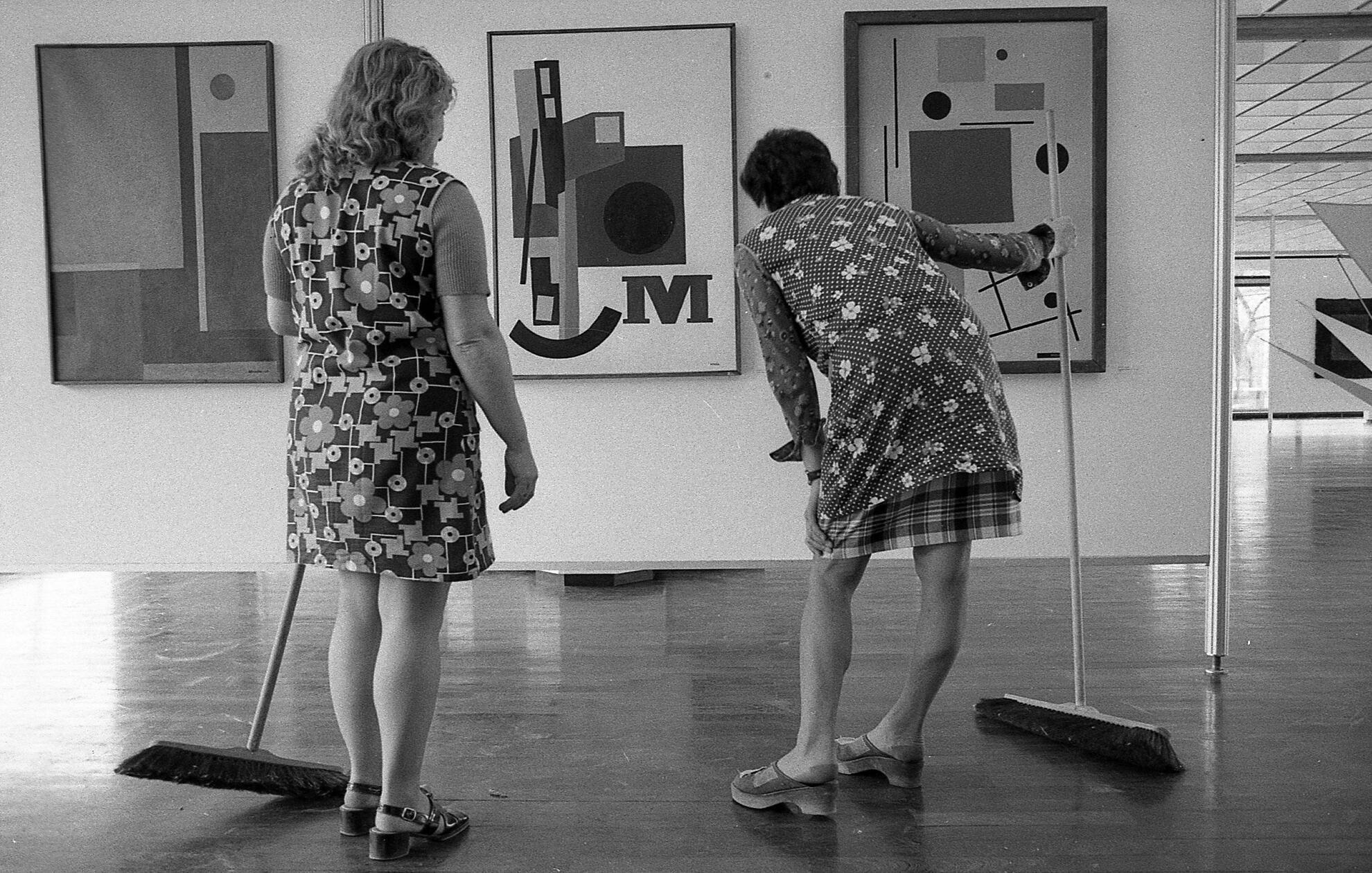 In Kunstbetrachtung versunken: Einen Moment der Muße gönnen sich zwei Raumpflegerinnen auf unserem Motiv aus dem Jahre 1975, welches seinerzeit unter dem Titel "Kunstpflege" erschienen ist. Ihre geblümten Arbeitskittel bilden einen reizvollen Kontrast zu den ausgestellten abstrakten Kunstwerken. Um welche Ausstellung es sich handelt, ist leider nicht bekannt.