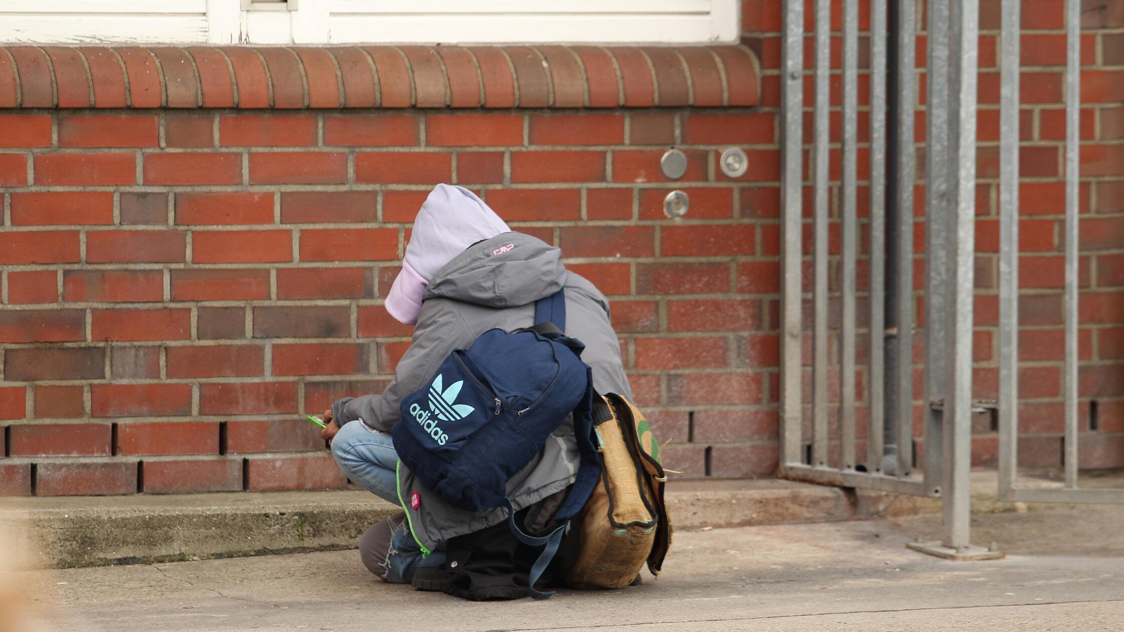 Eine drogenabhängige Frau sucht hinter einem Gebäu