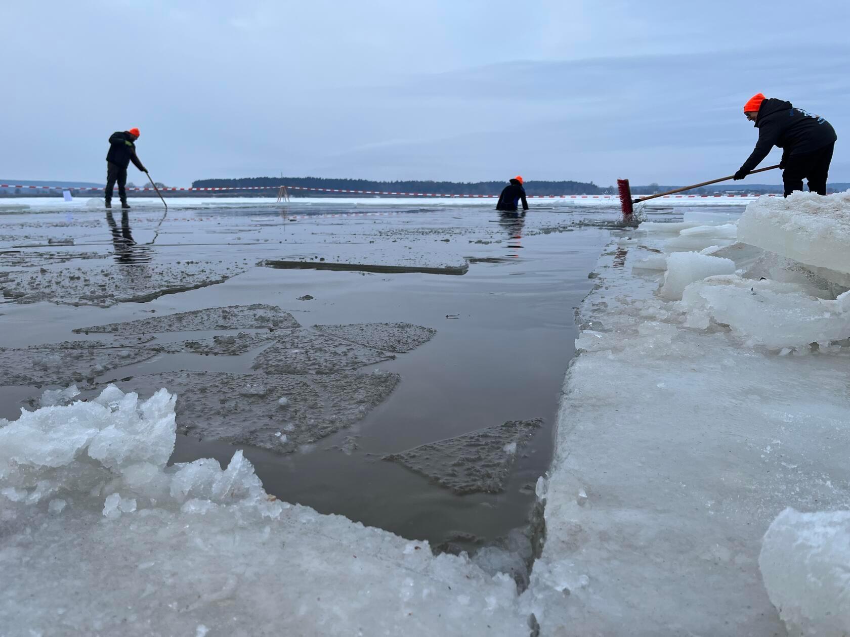 Damit am nächsten Tag überhaupt gebadet werden kann, rücken Helfer mit Kettensägen an. Die Eisdecke wird aufgeschnitten, ein großes Rechteck freigelegt.