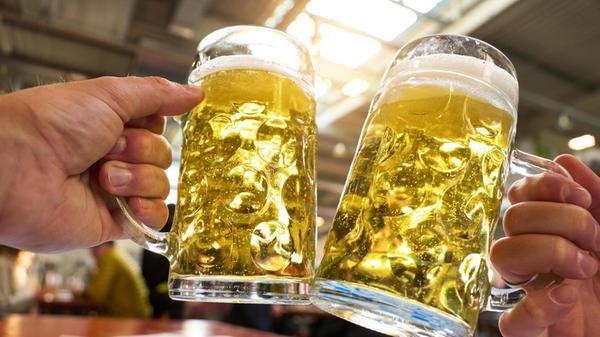 Zwei Männer stoßen mit vollen Bierkrügen an. Die G