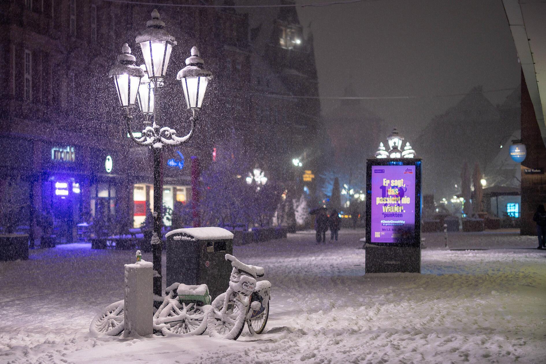 Zwei mit Schnee bedeckte Fahrräder stehen unter einer Laterne in der Innenstadt von Nürnberg.