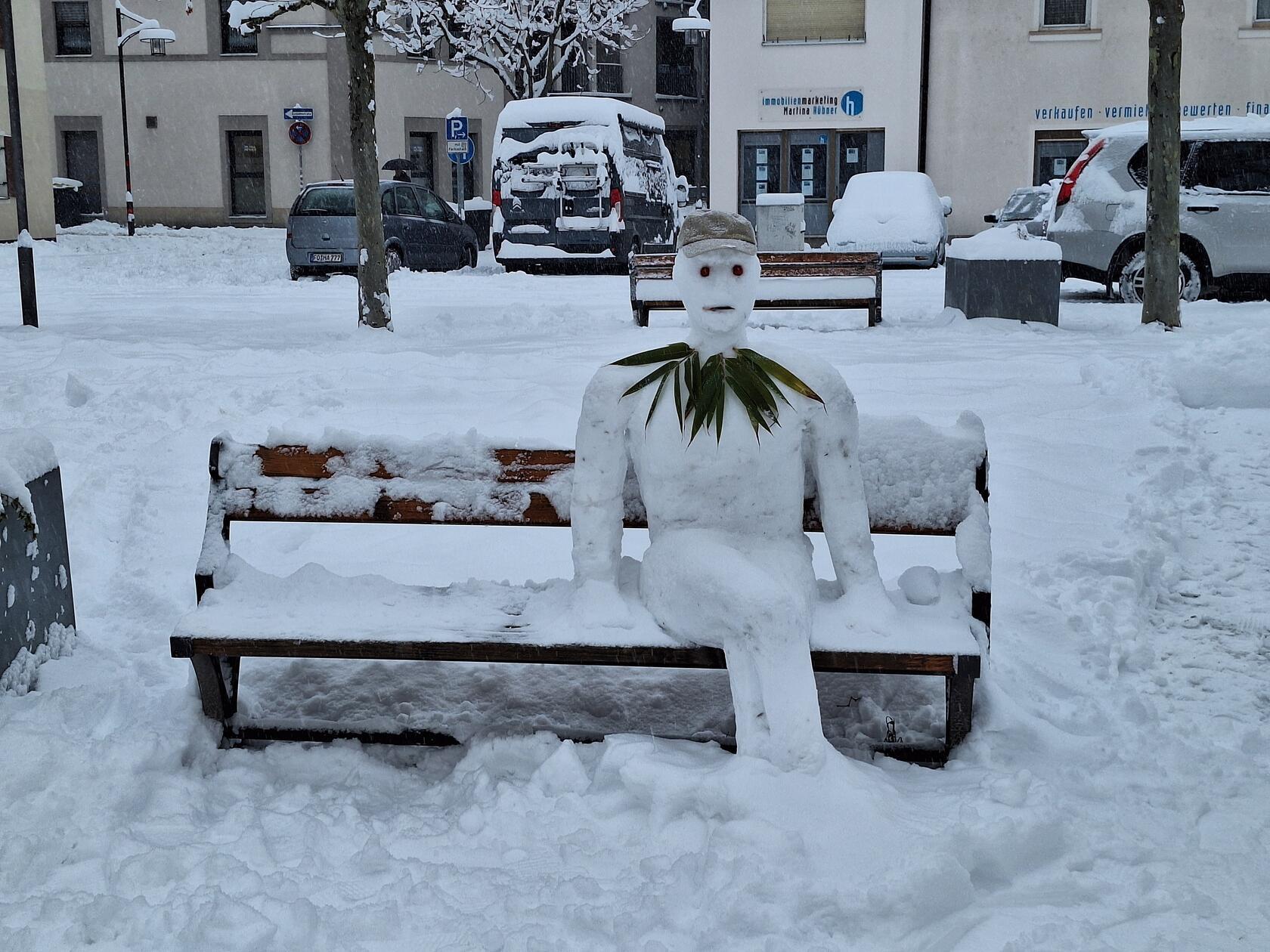 Schon am frühen Montagmorgen hat sich dieser Schneemann mit Tomatenaugen und Blätterkragen auf einer Bank am Forchheimer Marktplatz niedergelassen. Zahlreiche Passanten bleiben für ein Foto stehen.