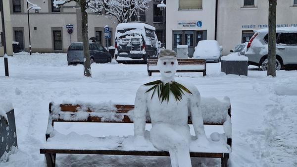 Schon am frühen Montagmorgen hat sich dieser Schneemann mit Tomatenaugen und Blätterkragen auf einer Bank am Forchheimer Marktplatz niedergelassen. Zahlreiche Passanten bleiben für ein Foto stehen.