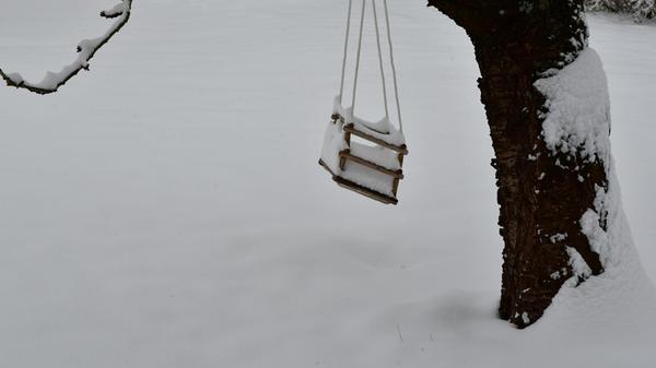 Kinder, die im sonnenüberfluteten Garten spielen und toben- daran erinnert diese eingeschneite Schaukel. In ein paar Wochen kann sie sicher wieder genutzt werden.