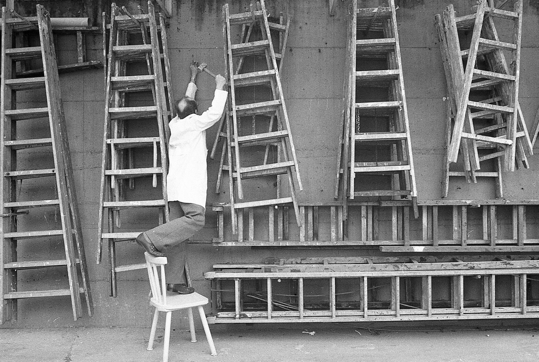 Wer hoch hinaus will, braucht gelegentlich eine Leiter. Aus einem reichhaltigen Fundus an gut sortierten Holzleitern könnte sich dieser ordnungsliebende Lagerist, wie unser Foto aus dem Jahr 1982 zeigt, durchaus bedienen, um einen Nagel in die Wand zu schlagen. Allerdings schien ihm die Benutzung einer Leiter wohl nicht das geeignete Mittel der Wahl gewesen zu sein. Es bleibt zu hoffen, dass sein waghalsiger Balance-Akt auf dem Stuhl keinen Fehltritt zur Folge hatte.