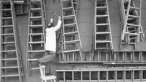 Wer hoch hinaus will, braucht gelegentlich eine Leiter. Aus einem reichhaltigen Fundus an gut sortierten Holzleitern könnte sich dieser ordnungsliebende Lagerist, wie unser Foto aus dem Jahr 1982 zeigt, durchaus bedienen, um einen Nagel in die Wand zu schlagen. Allerdings schien ihm die Benutzung einer Leiter wohl nicht das geeignete Mittel der Wahl gewesen zu sein. Es bleibt zu hoffen, dass sein waghalsiger Balance-Akt auf dem Stuhl keinen Fehltritt zur Folge hatte.
