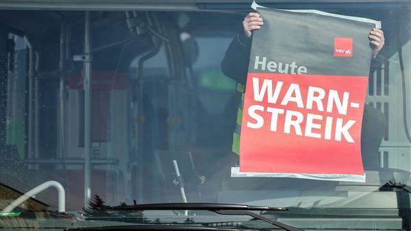 Ein Mitarbeiter befestigt ein Warnstreik-Plakat wä