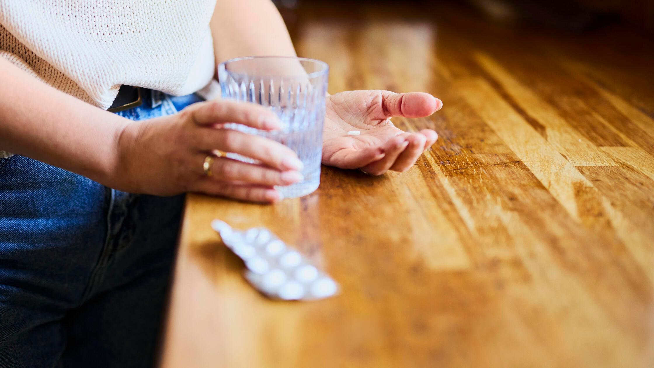 Woman holding water and pills in kitchen close up 