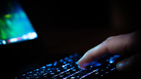 Hand auf einer Laptop Tastatur in einem dunklen Ra