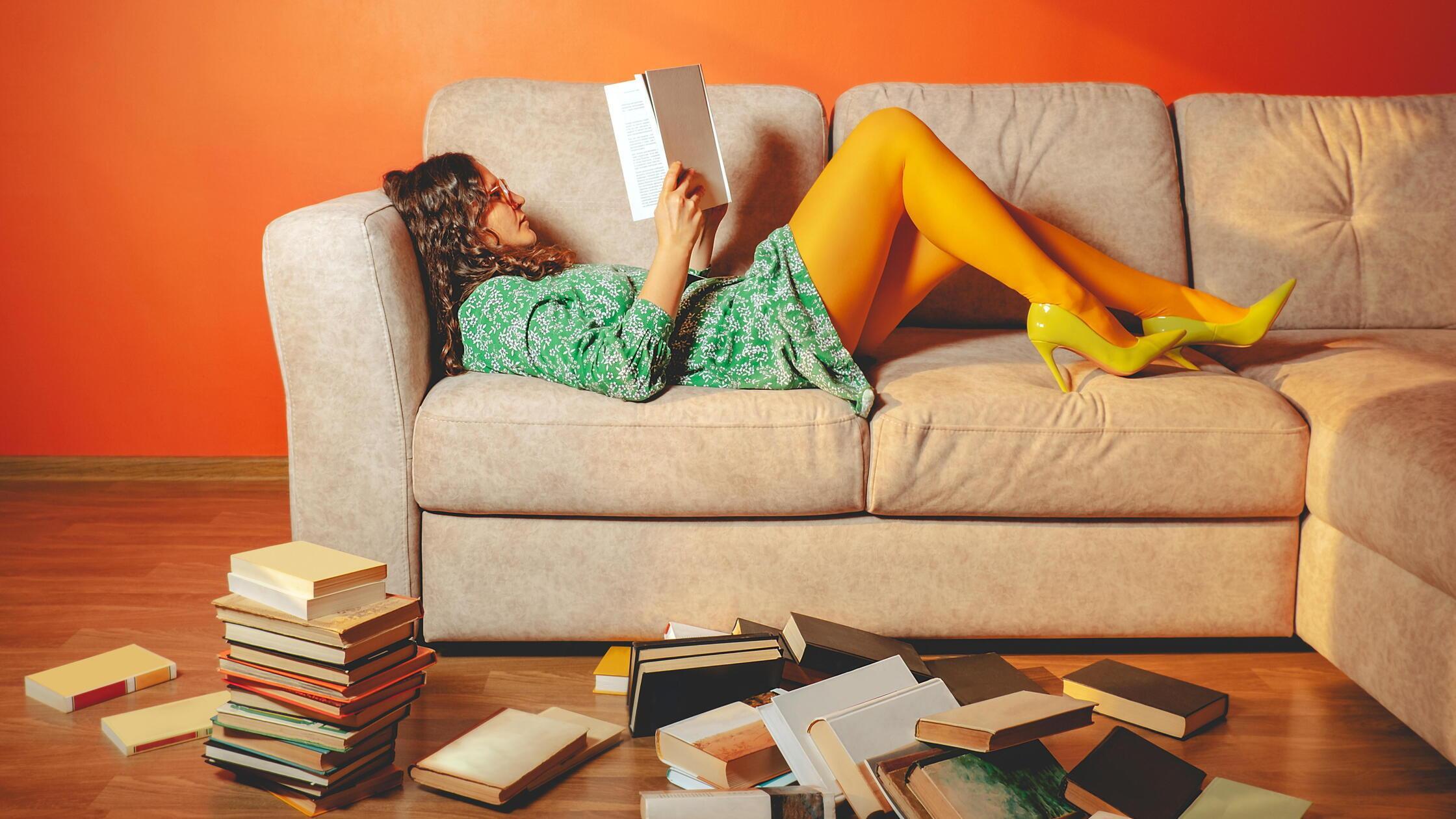 Person relaxing on sofa reading book in bright liv