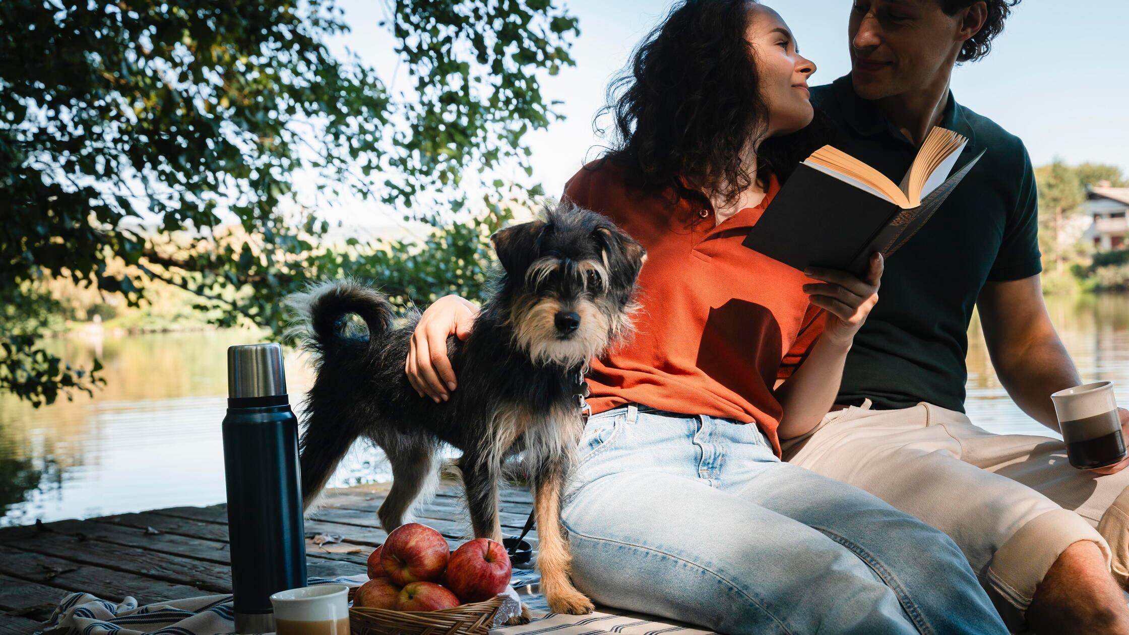 Couple relaxing with dog and picnic by the lake ou