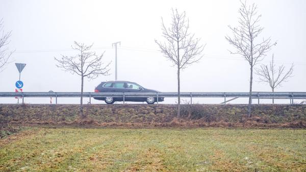 Ein Auto fährt über eine Straße im Nebel. Der Sonn