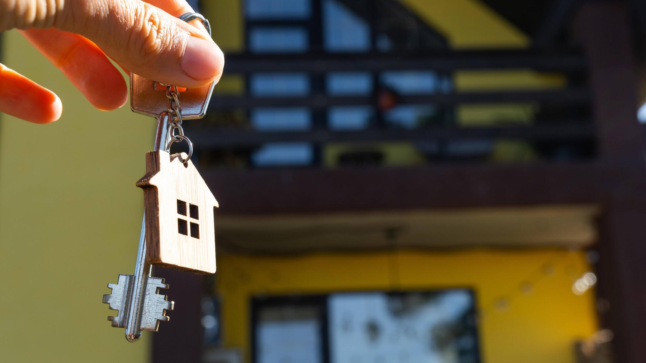 Schlüssel zum Haus mit winzigem Haus in Händen von