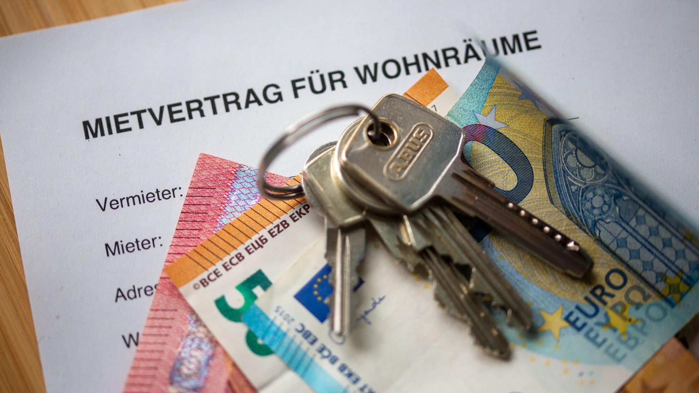 Auf einem Mietvertrag liegen Geldscheine und ein H