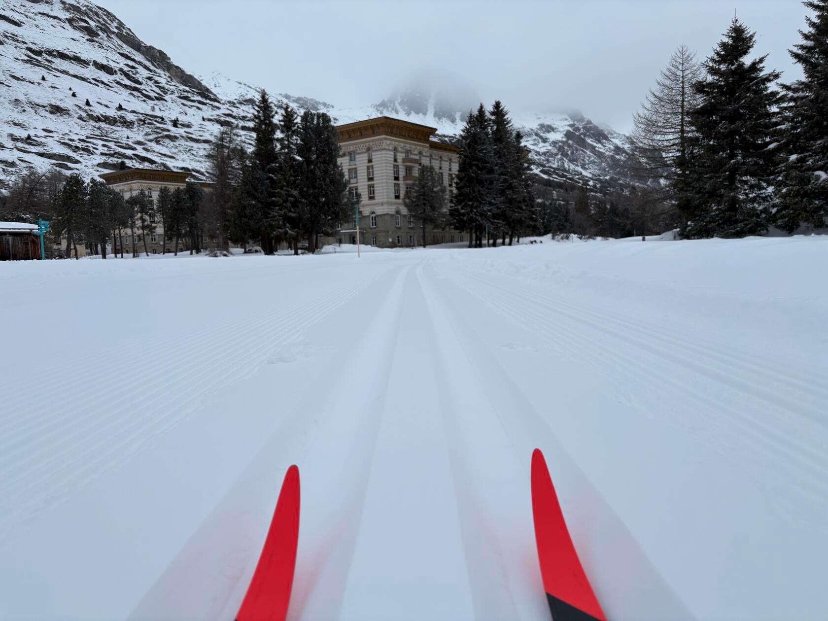 Die Skispitzen laufen in Maloja einem Hotel entgegen - dahinter erstreckt sich der Silser See, über den die Loipe führt.