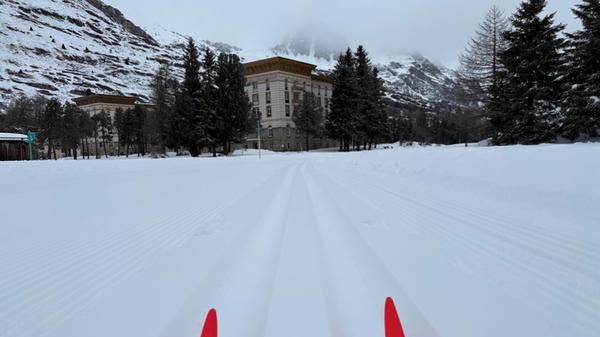 Die Skispitzen laufen in Maloja einem Hotel entgegen - dahinter erstreckt sich der Silser See, über den die Loipe führt.