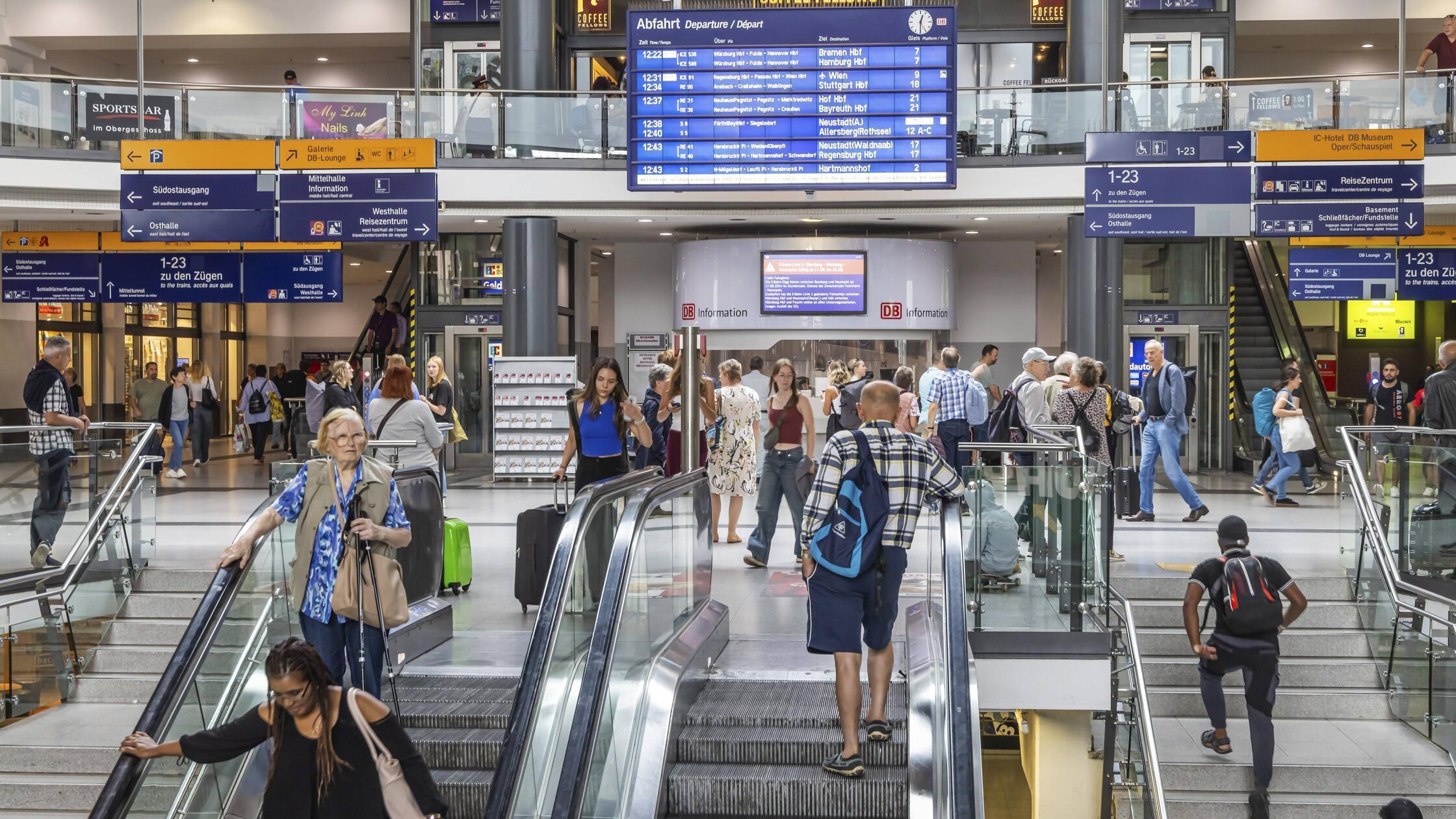 Reisende im Bahnhofsgebäude mit Läden und digitale