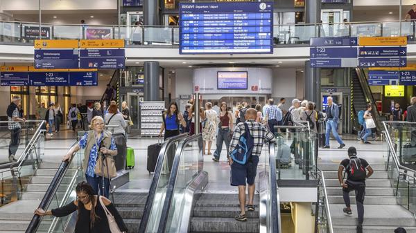 Reisende im Bahnhofsgebäude mit Läden und digitale