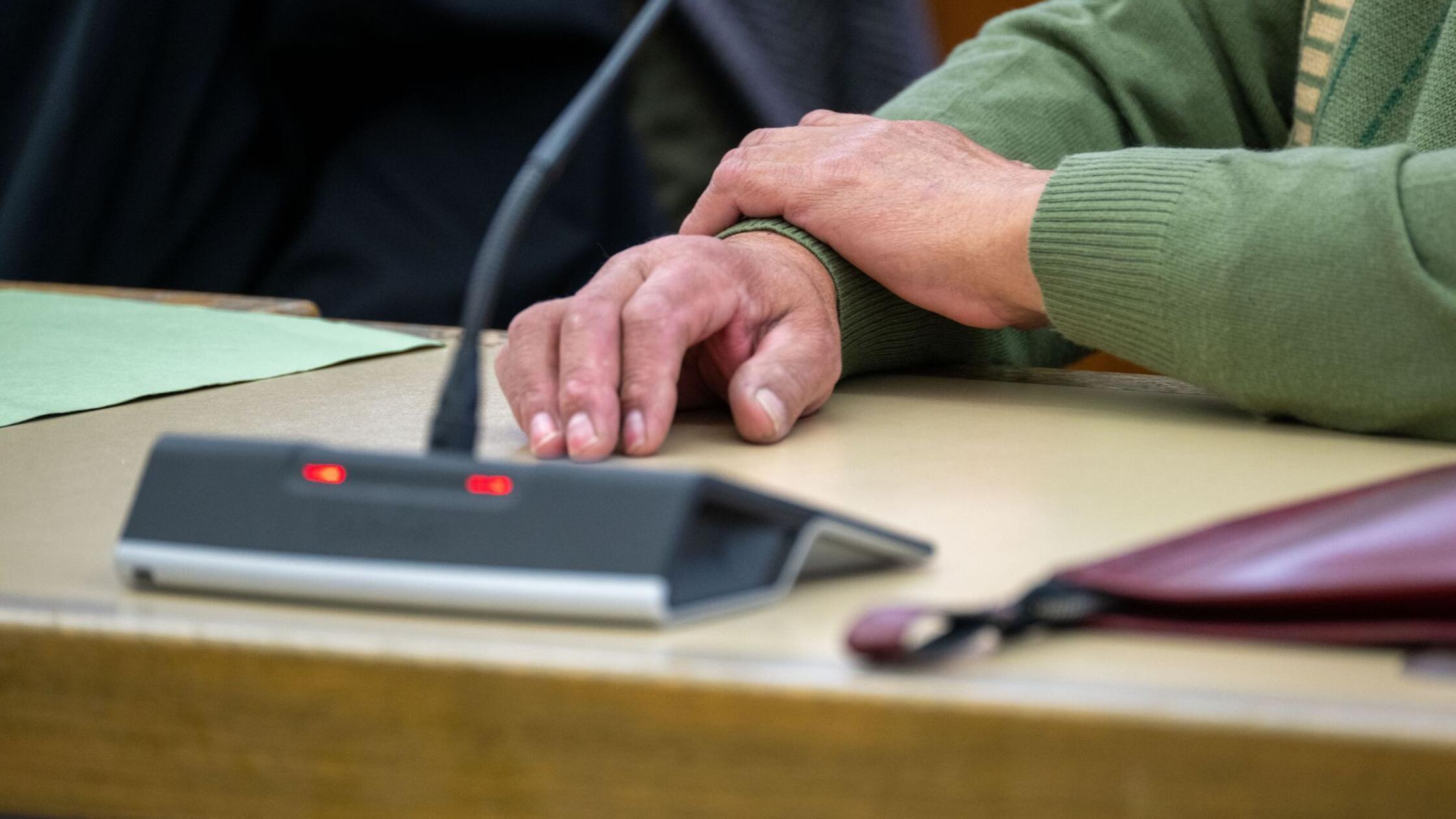 Mit beiden Händen auf dem Tisch wartet der Angekla