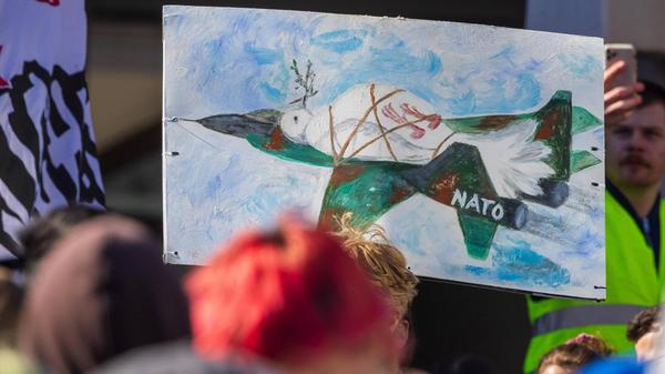 Viele Jugendliche haben eigene Plakate mitgebracht. Ein besonders auffälliges Demonstrationsplakat zeigt etwa eine gemalte Friedenstaube, die mit einer Kette an ein Kampfflugzeug gefesselt ist.