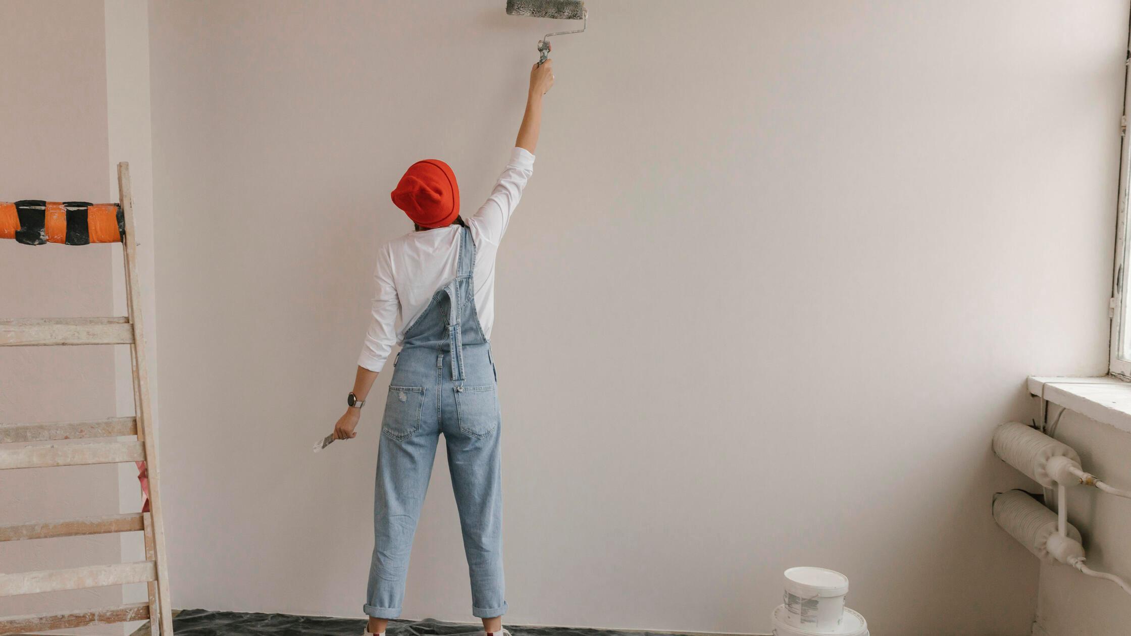 Woman using paint roller on white wall at new home