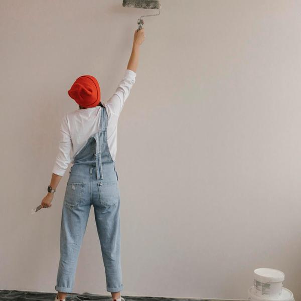 Woman using paint roller on white wall at new home