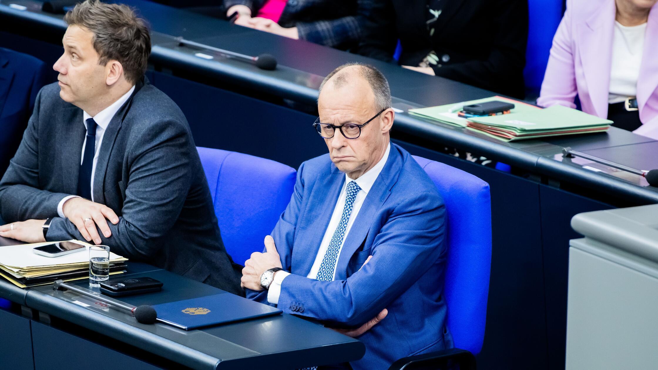 Bundeskanzler Friedrich Merz (CDU, M) sitzt neben 