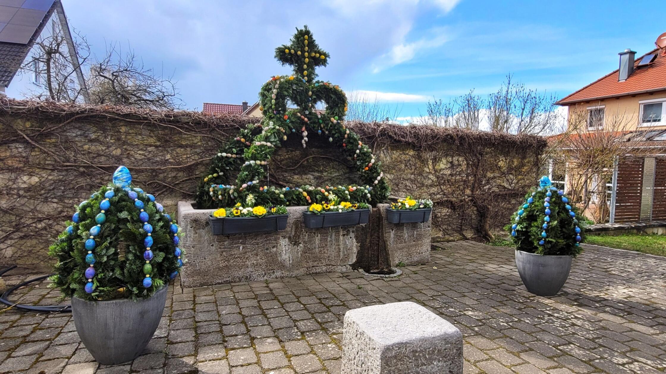 Vor der historischen Kulisse des Schlosses Wiesenthau, einem Renaissancebau aus der Mitte des 16. Jahrhunderts, zeigt sich der kunstvoll geschmückte Brunnen in traditioneller fränkischer Ausgestaltung.
