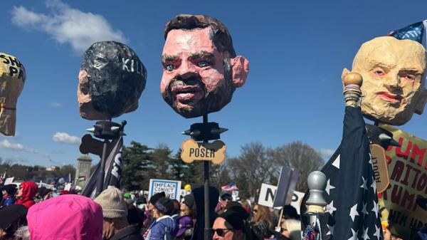 Demonstrierende tragen Pappköpfe, die u.a. den US-