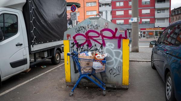 Ein Einkaufswagen voller Müll steht an einem Glasc
