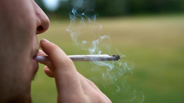 Ein Jugendlicher zieht an einem Cannabis Joint. Sy