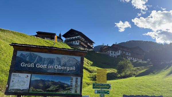Willkommen in Obergail: Das Begrüßungsschild am Ortseingang mit Blick auf die saftigen Almwiesen und den idyllischen Weiler.