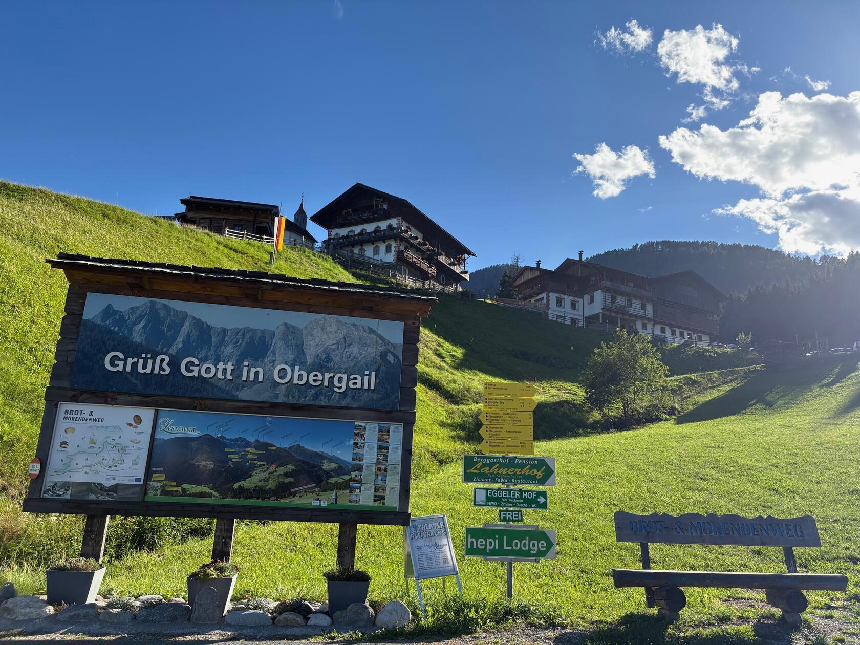 Willkommen in Obergail: Das Begrüßungsschild am Ortseingang mit Blick auf die saftigen Almwiesen und den idyllischen Weiler.