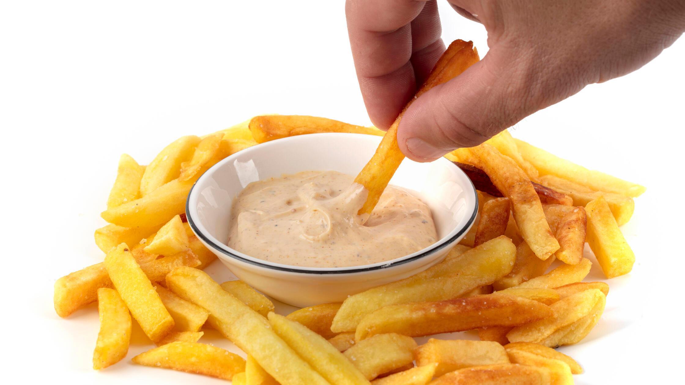 Eine Hand taucht Pommes frites in eine weiße Schal