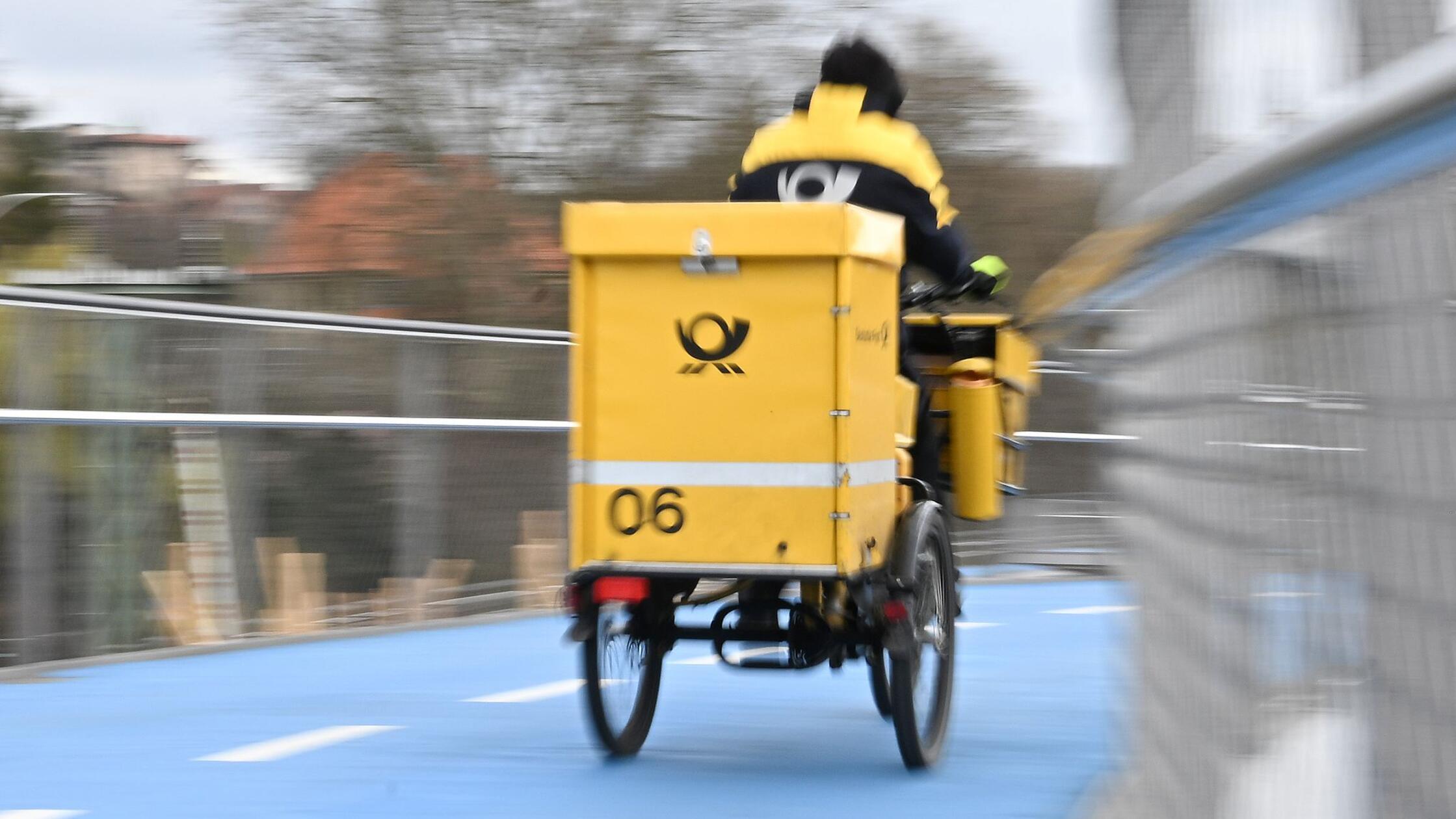 Ein Briefausträger der Post fährt mit einem Rad üb