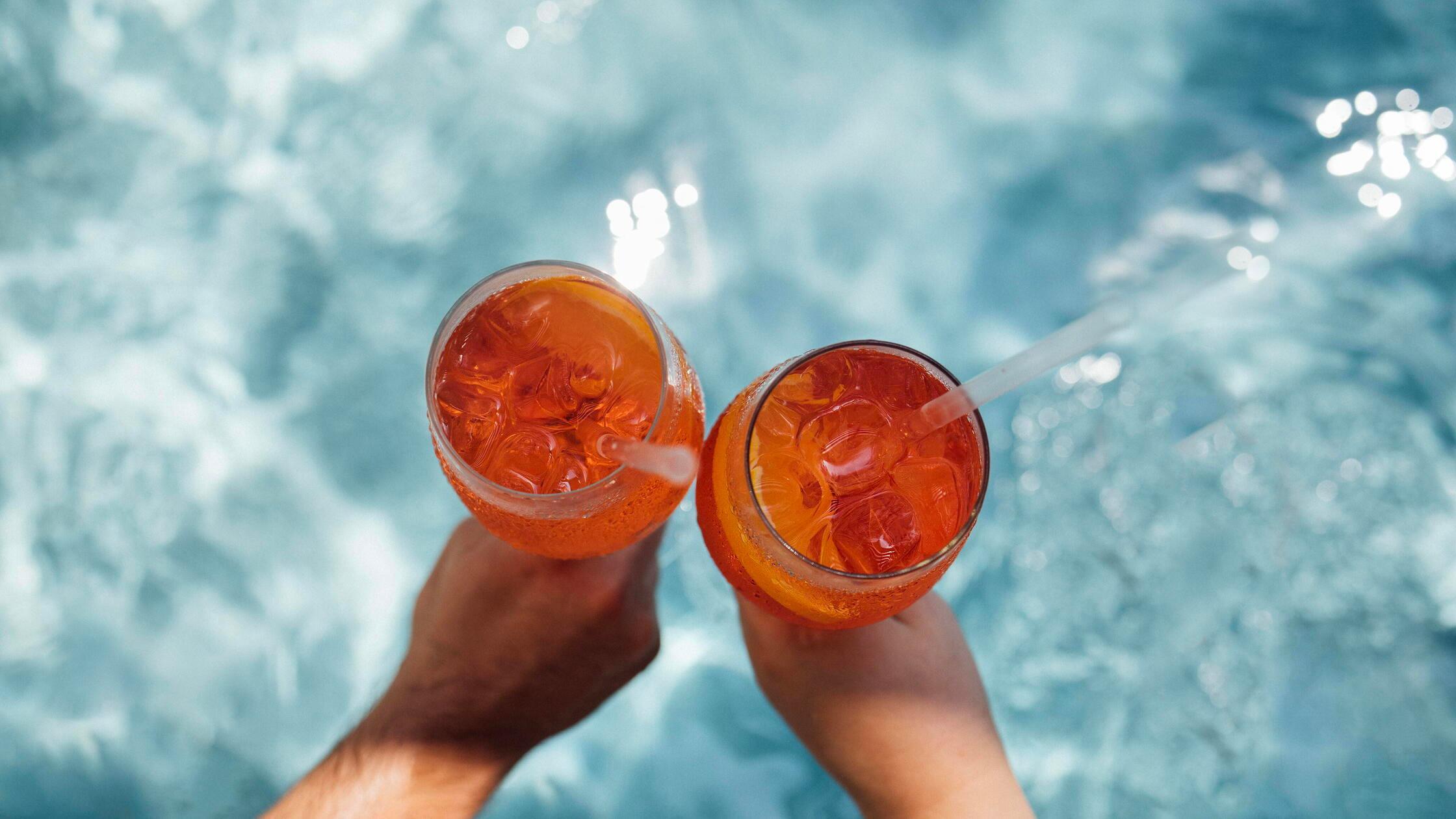 Zwei Hände halten Gläser mit orangefarbenen Cockta