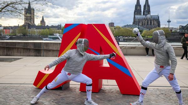 Zwei Fechter kämpfen vor dem Schriftzug „JA“ auf d