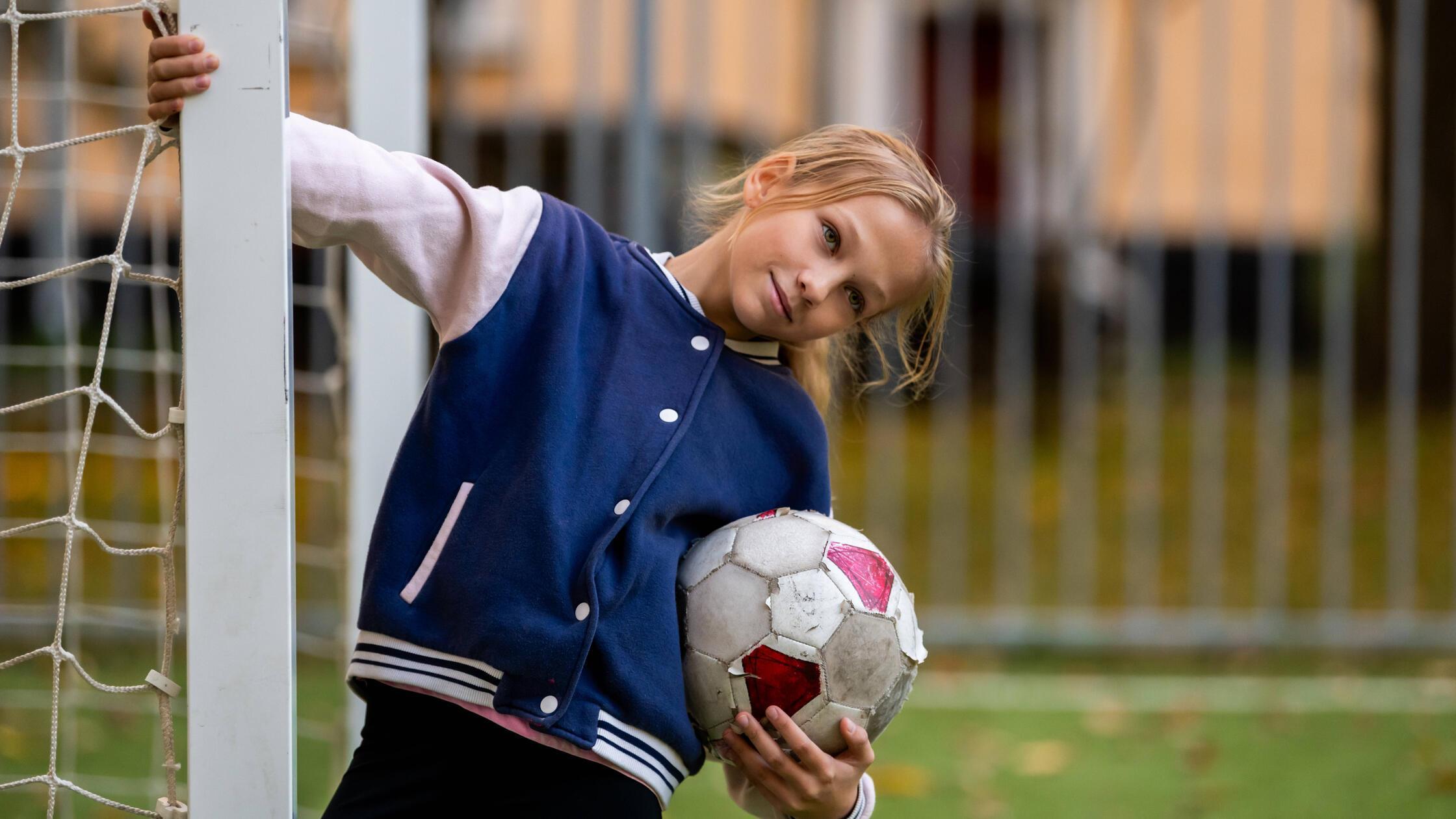 girl is holding a soccer ball on a soccer field in