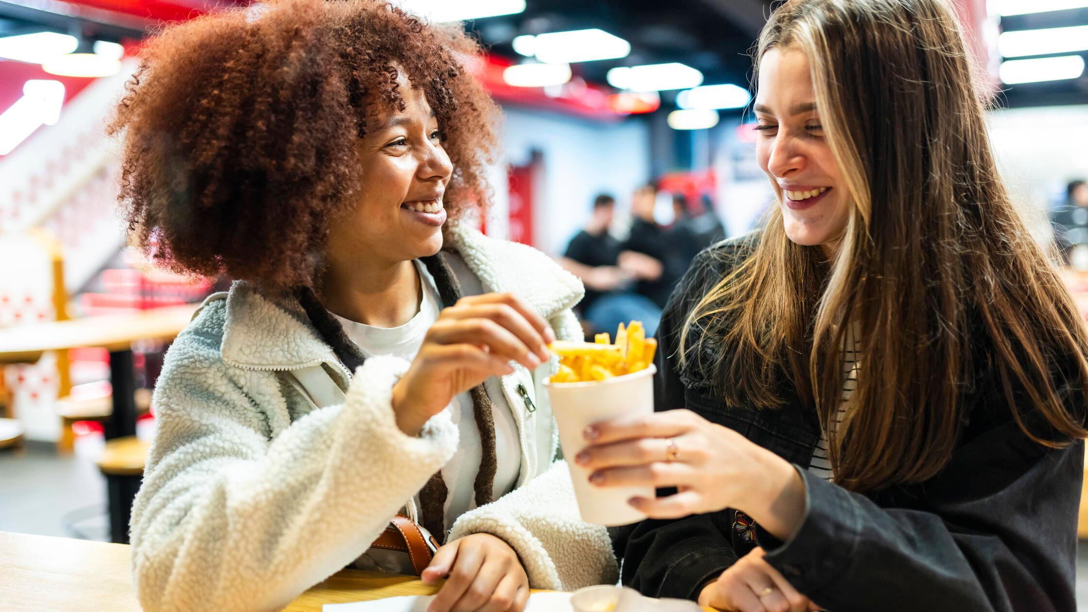 Happy young friends sharing french fries in cafe m