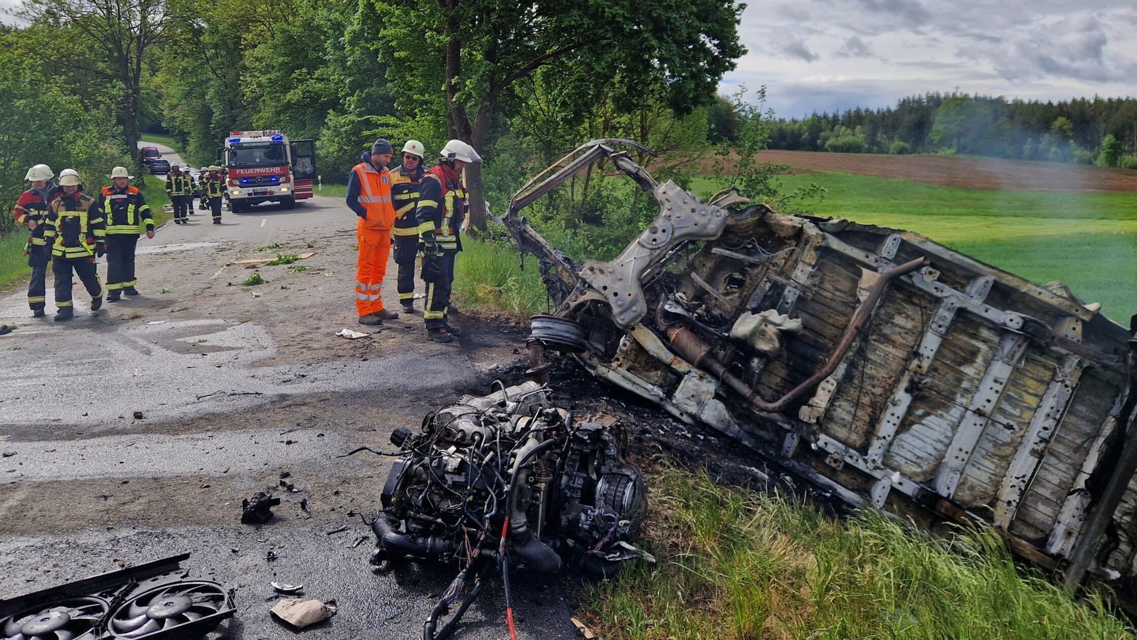 Feuerwehrleute stehen an dem ausgebrannten Wrack e