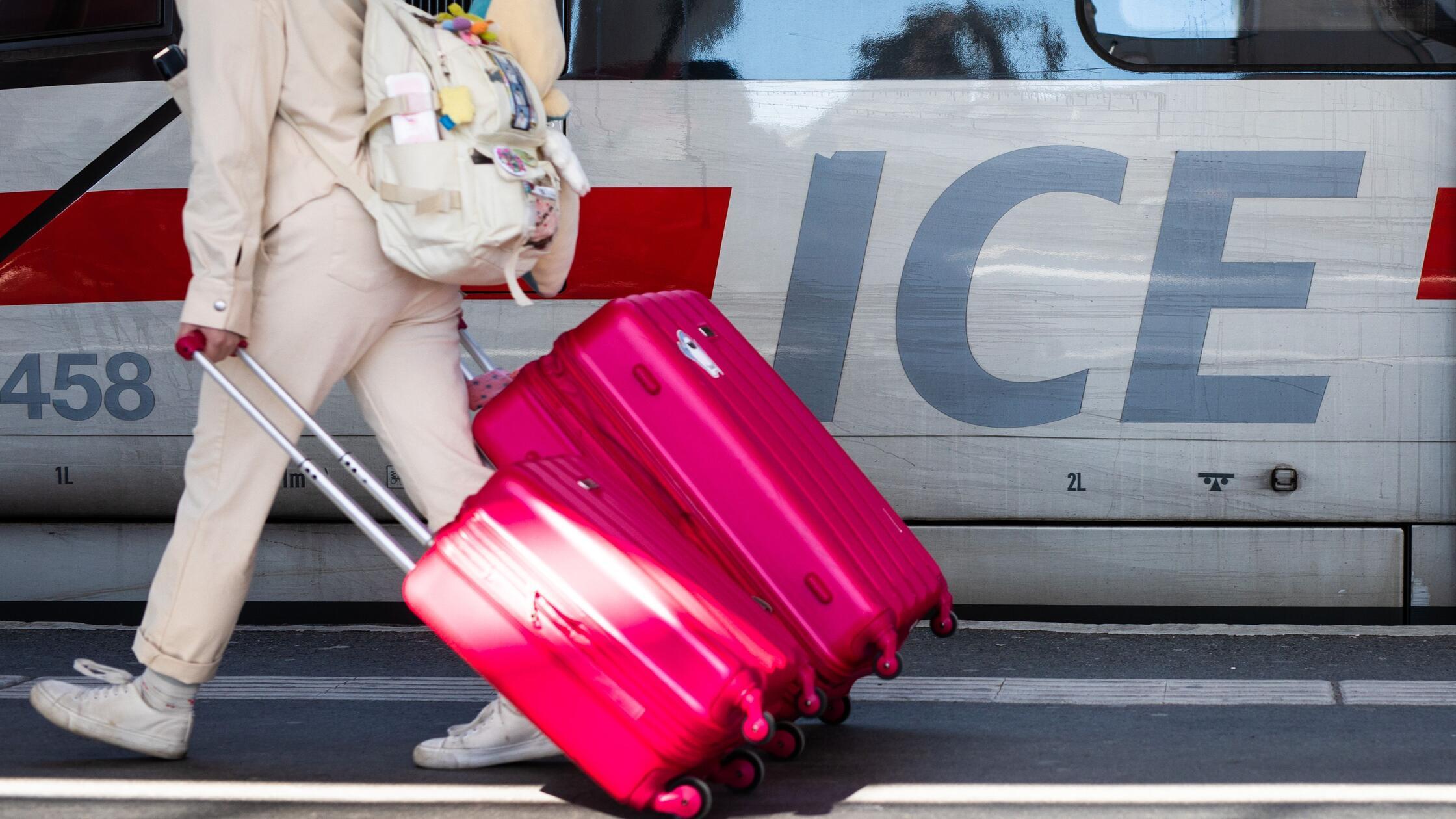 Eine Frau läuft mit ihren Koffern an einem ICE-Zug