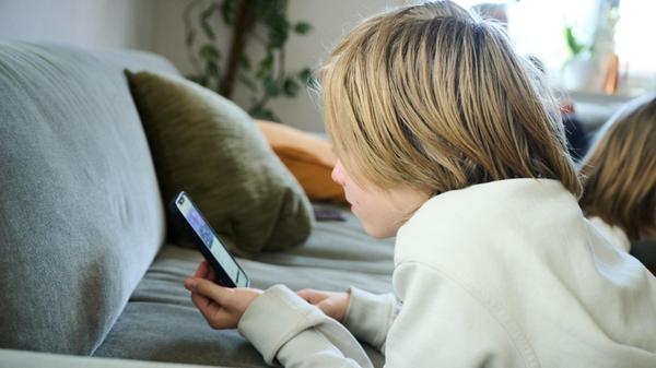 Ein Junge liegt auf einem Sofa und blickt auf sein