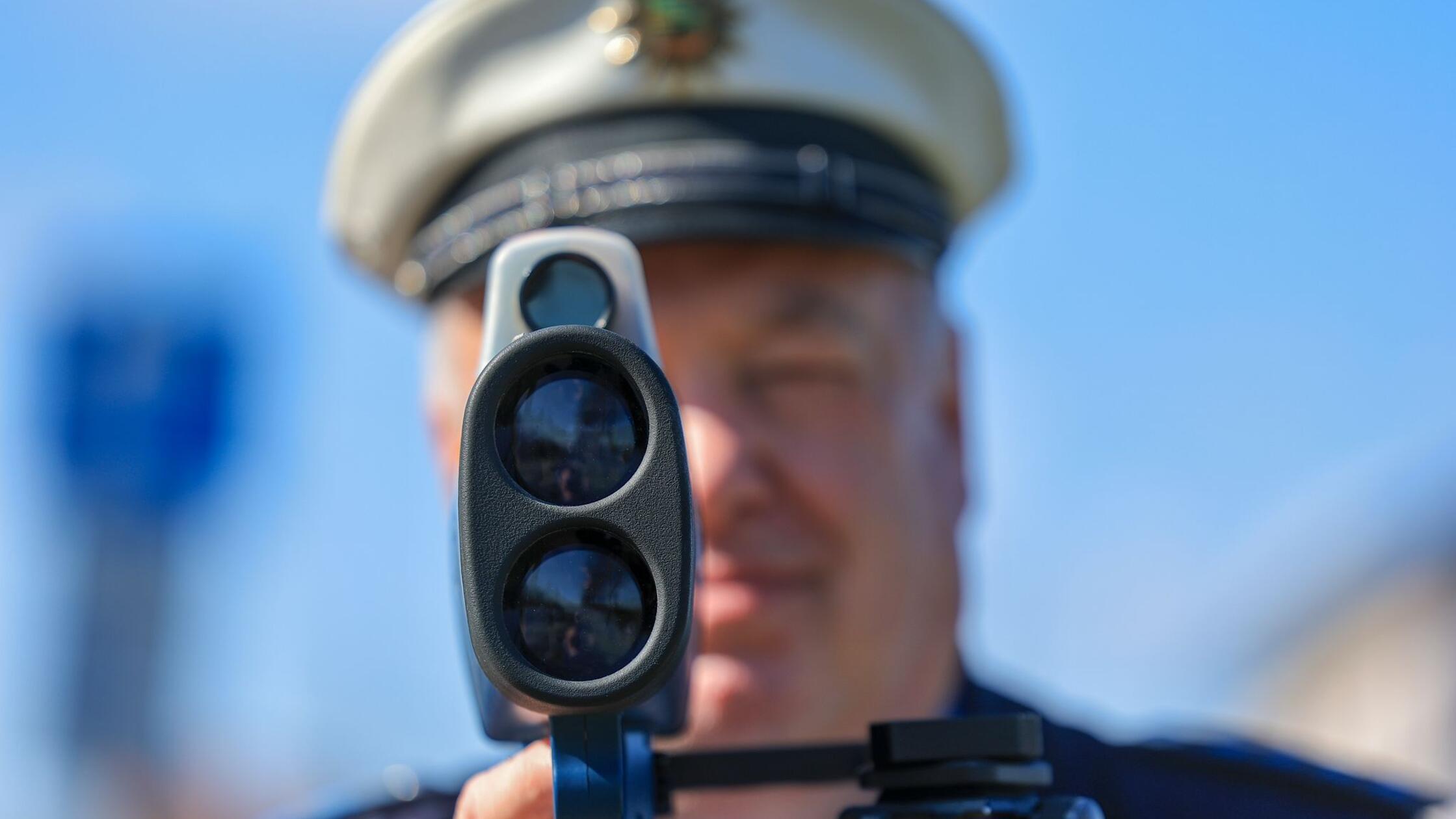Ein Polizist misst mit einem Laserhandmessgerät (L
