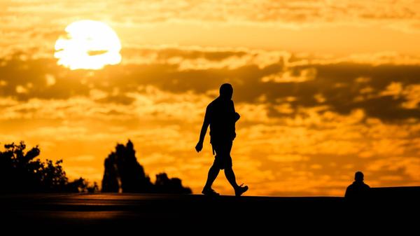 Ein Mann geht bei Sonnenaufgang über eine Straße i
