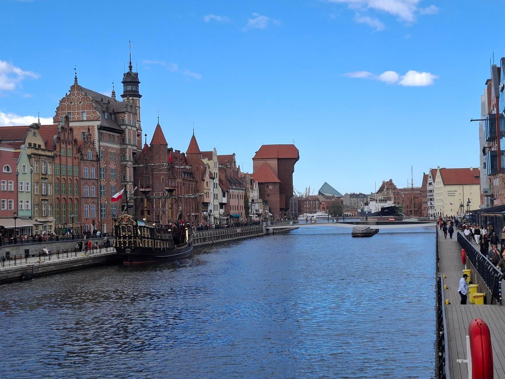 Danzig (polnisch: Gdańsk) ist eine über 1000 Jahre alte Hansestadt an der polnischen Ostseeküste und bildet zusammen mit Sopot und Gdynia die Metropolregion „Dreistadt“ (Trójmiasto). Sie ist weltberühmt für ihre rekonstruierte Rechtstadt, ihre Rolle als Schauplatz des Beginns des Zweiten Weltkriegs sowie als Wiege der Gewerkschaftsbewegung Solidarność, die maßgeblich zum Fall des Kommunismus in Europa beitrug. Hier die Häuserzeile mit dem Krantor im Hintergrund entlang der Mottlau. Im Vordergrund ein Pratenschiff, auf dem Touristen auf dem Fluss bis zur Ostsee fahren können und einiges über die Stadt erfahren.