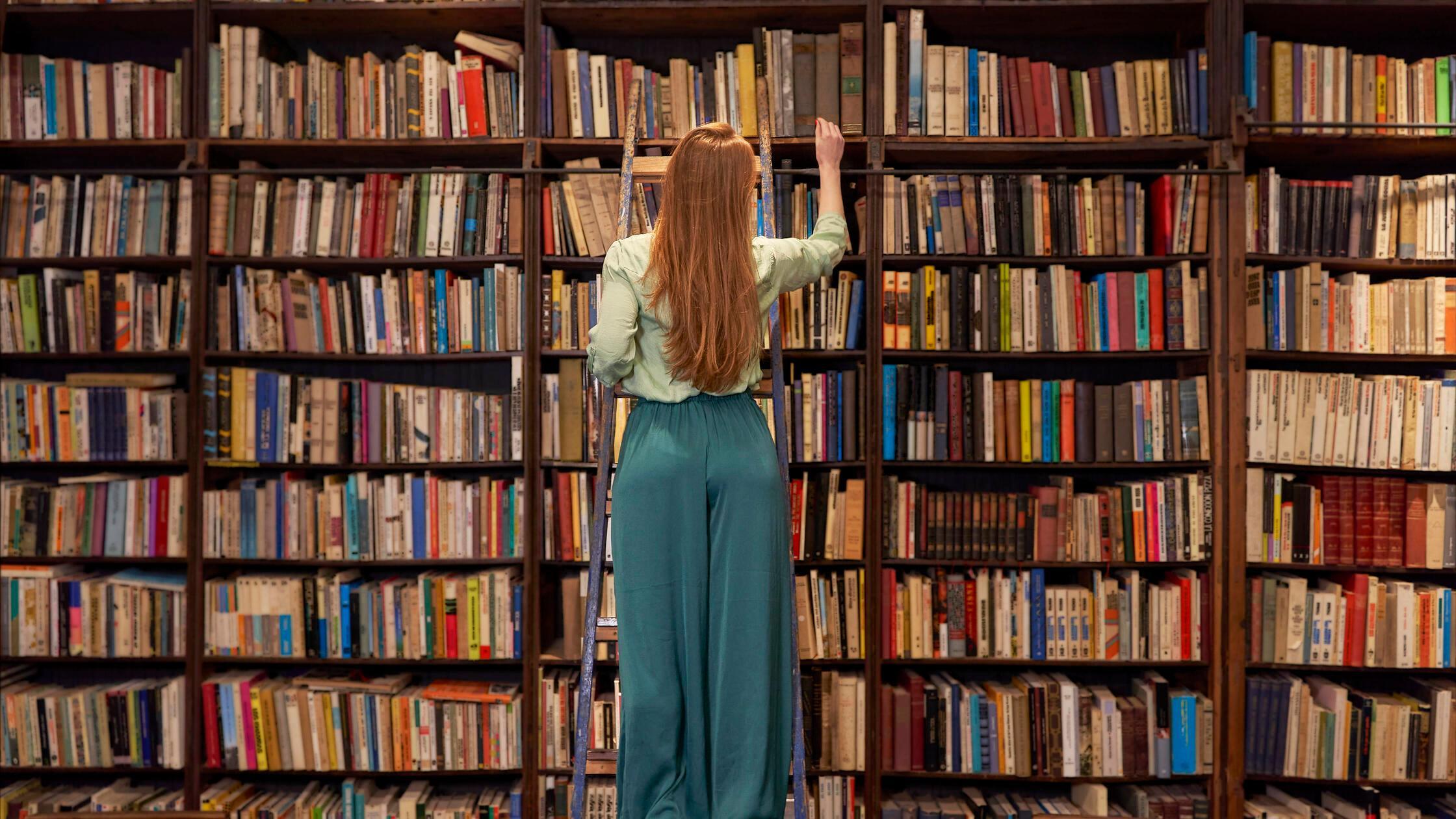 Young woman standing on ladder while searching boo