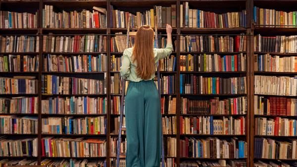 Young woman standing on ladder while searching boo