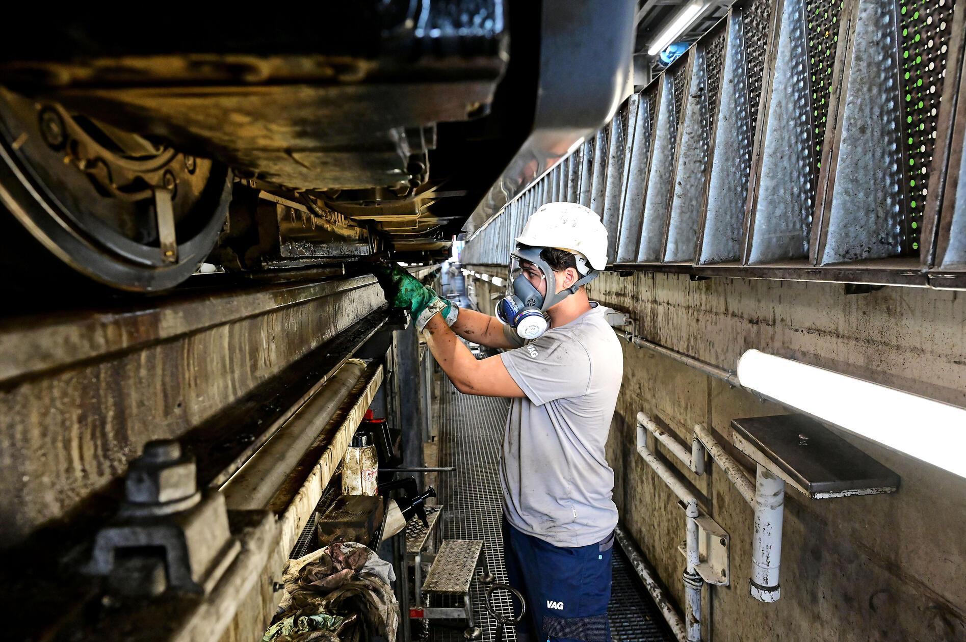 In der Werkstatt Straßenbahnbetriebshof Heinrich-Alfes-Straße beseitigen Mitarbeiter die Reste von Bitumen auf Rädern und Bremsen. Hier sind rund 70 Angestellte mit Schutzausrüstung unter den Straßenbahnen zugange.