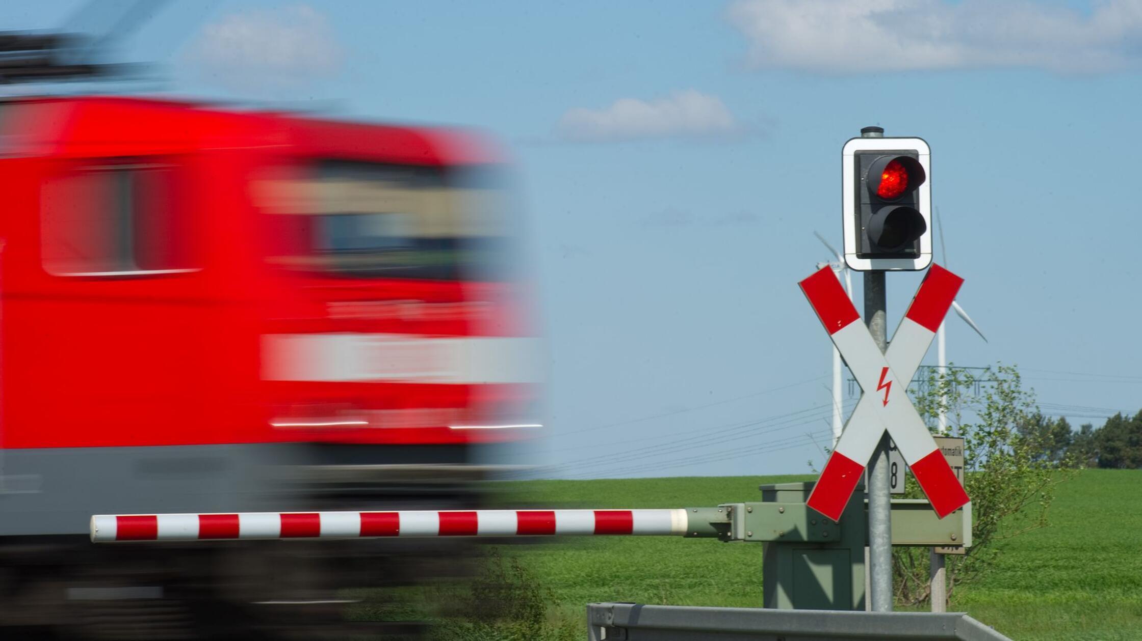 Ein Zug fährt an einem geschlossenem Bahnübergang 